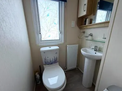 a bathroom with a toilet and a sink and a window at Lovely 6 Berth Caravan With Decking At Suffolk Sands Holiday Park Ref 45005Hc in Felixstowe