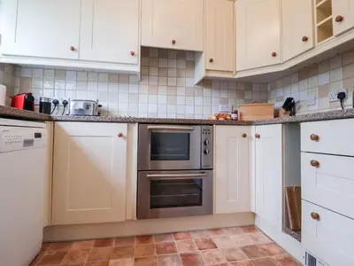 a kitchen with white cabinets and an oven at Bay Tree Cottage in Saxmundham