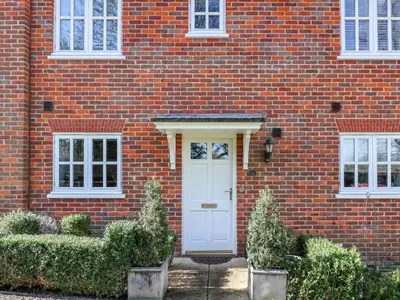 a brick house with a white door and bushes at Bay Tree Cottage in Saxmundham