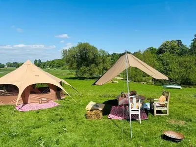 two tents in a field with people sitting in chairs at Riverside farm Yurt tent Hertford in Hertford