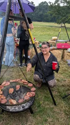 a woman is cooking food on a grill at Farm woodland riverview cabin bbq firepit pet friendly in Hertford