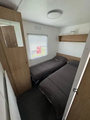 a small room with two beds and a door at Seawick Holiday Park Caravan Hire in Saint Osyth