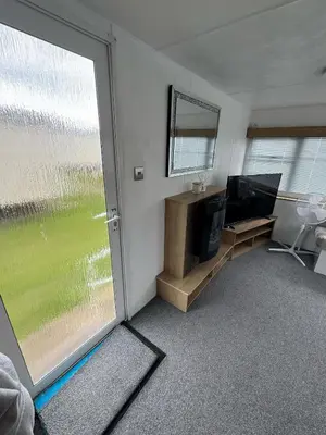 a room with a tv and a sliding glass door at Seawick Holiday Park Caravan Hire in Saint Osyth
