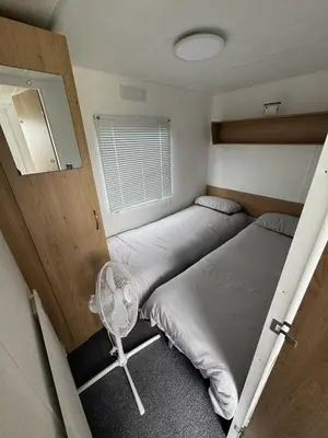 a small bedroom with two beds and a fan at Seawick Holiday Park Caravan Hire in Saint Osyth