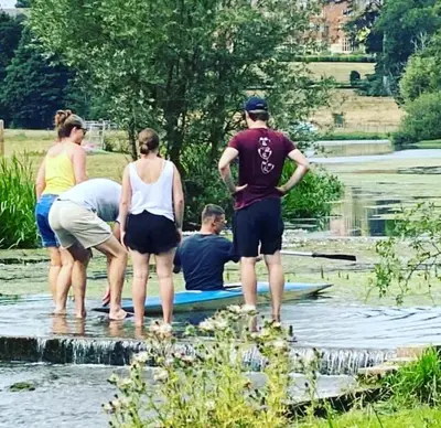 a group of people standing on a surfboard in the water at Hertford belltent farm stay riverside firepit bbq in Hertford