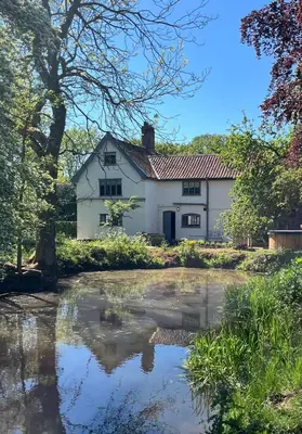 a white house with a reflection in a pond at Park Farm in Thornham Magna