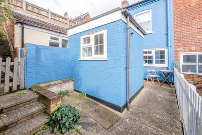 a blue tiny house in front of a brick building at Stones Throw, Aldeburgh in Aldeburgh