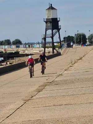 two people riding bikes down a boardwalk near a lighthouse at Alices’s Beachside Haven in Harwich