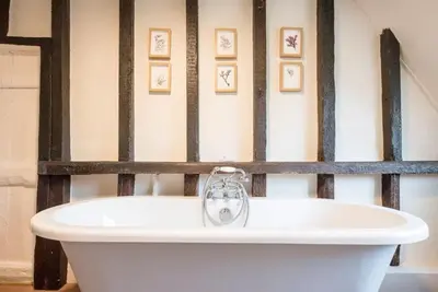 a white bath tub in a bathroom with pictures on the wall at The Old Cottage - Sudbourne, near Orford in Sudbourne