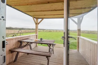 a wooden porch with a picnic table and a view of a field at River Lodge, Aldeburgh in Aldeburgh