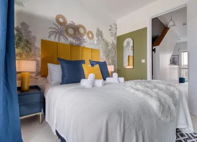 a bedroom with a large bed with blue and yellow pillows at Cambridge - hot tub, sauna, parking, pool table in Trumpington