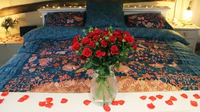 a vase with red roses on a table in front of a bed at Chinnerys Country Cottage in Cavendish