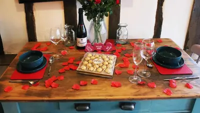 a table with wine glasses and red flowers on it at Chinnerys Country Cottage in Cavendish