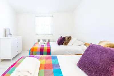a white bedroom with two beds and purple pillows at Edinburgh House in Aldeburgh