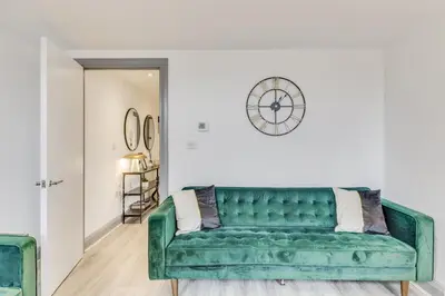 a green couch in a living room with a clock on the wall at Stylish stay Ware town with parking in Ware