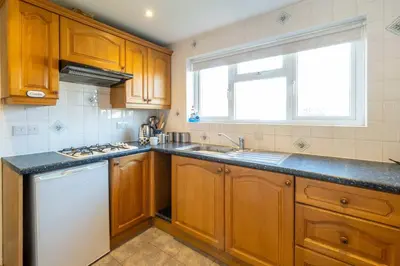 a kitchen with wooden cabinets and a white dishwasher at 6 Franklin Rd - Aldeburgh Coastal Cottages in Aldeburgh