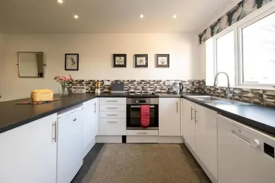a kitchen with white cabinets and black counter tops at 51 The Plantation - Aldeburgh Coastal Cottages in Aldeburgh