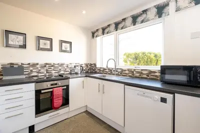 a kitchen with white cabinets and a large window at 51 The Plantation - Aldeburgh Coastal Cottages in Aldeburgh