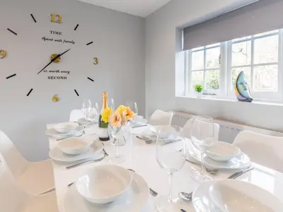 a white dining room with a table and clocks on the wall at 4-Bedroom Seafront House in Southend Sea Views - Pass the Keys in Southend-on-Sea