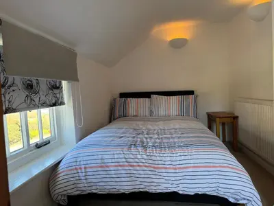 a bedroom with a bed with a striped comforter and two windows at Cosy Little Cottage in Woodbridge