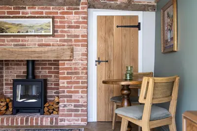 a brick fireplace next to a table and a door at Ruperts Cottage in Coggeshall