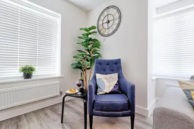 a blue chair in a living room with a clock on the wall at Spacious Colchester Home with Off-Street Parking for 4 cars in Colchester