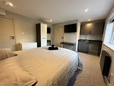 a bedroom with a large white bed and a kitchen at Abbey Rooms in Waltham Abbey