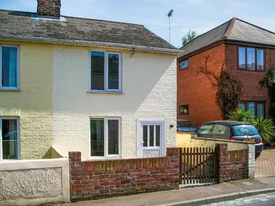 a white house with a brick fence next to a house at Cosy Cottage in Manningtree