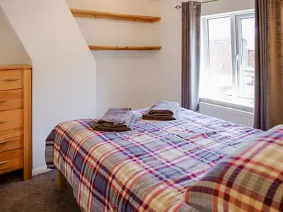 a bedroom with a bed with a plaid blanket and a window at Cosy Cottage in Manningtree