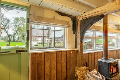 a wood paneled room with a stove and windows at The Dairy at Green Valley Farm in Laxfield