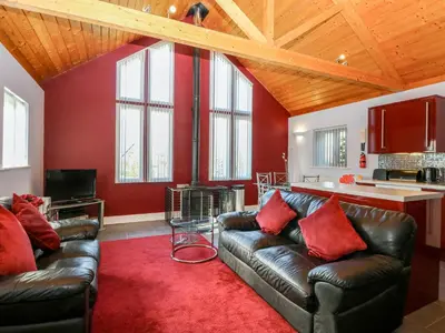 a living room with leather couches and a red wall at Rookyard Cottage in Halesworth