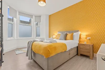 a bedroom with a large bed and a yellow wall at Cozy accessible 2bd flat on Mill road with firepit for a lovely winters night in Cambridge