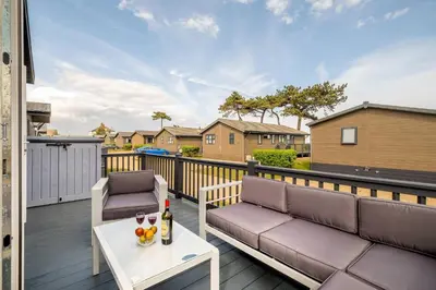 a patio with a couch and a table on a deck at Driftwood Lodge, Sizewell - Adults only property - Aldeburgh Coastal Cottages in Sizewell