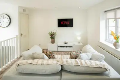 a living room with a couch and a clock on the wall at Loughton Hideaway: Cozy 1BD Near Tube & Nature in Theydon Bois