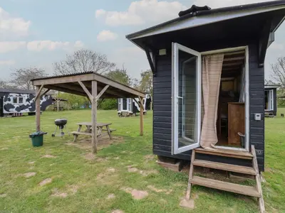 a black tiny house with a porch and a grill at Betsy Cow Shed 2 in Woodbridge