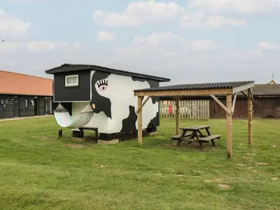 a building with a cow painted on it next to a picnic table at Bluebelle Cow Shed 5 in Woodbridge