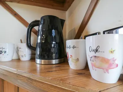 a row of coffee mugs sitting on a wooden shelf at Daisy Cow Shed 1 in Woodbridge