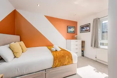a bedroom with a bed with an orange accent wall at Modern Spacious 4 Bedroom 3 Bathroom House by Trinity Stays Short Term Lets & Serviced Accommodation Cambridge in Cambridge