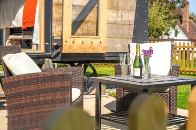 a table with two chairs and a table with wine bottles at Gin and Toffee Carriage in Thaxted