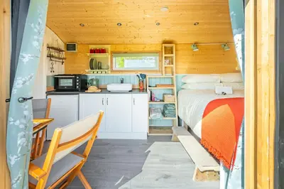 a bedroom in a tiny house with a bed and a kitchen at Gin and Toffee Carriage in Thaxted