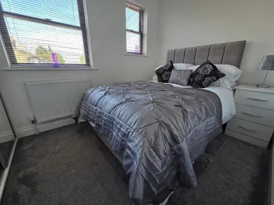a bedroom with a bed with a gray comforter and two windows at Promenade Apartment in Maldon