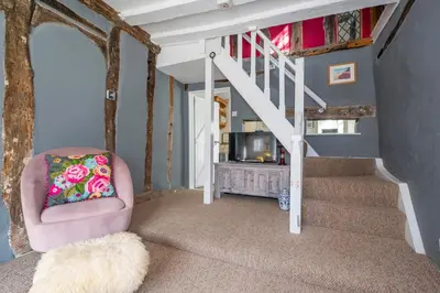 a living room with a chair and a staircase at Hylton Cottage, Lavenham in Lavenham