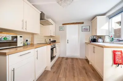 a kitchen with white cabinets and wooden floors at Hylton Cottage, Lavenham in Lavenham