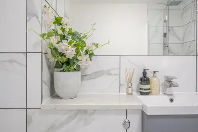 a white bathroom with a vase with flowers on a shelf at 2 Luxurious Apartments with Free Parking near Chelmsford City in Chelmsford