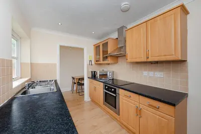 a kitchen with wooden cabinets and a black counter top at Spacious 3 bed flat in Colchester - Free parking in Hythe