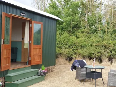 a green shed with a table and chairs outside at Delightful shepherd's hut in a rural location in North Fambridge