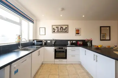 a kitchen with white cabinets and a sink and a window at 7 The Plantation - Aldeburgh Coastal Cottages in Aldeburgh