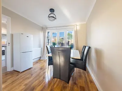 a dining room with a table and chairs and a refrigerator at Urban Ease Basildon in Basildon