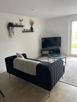 a living room with a black couch and a tv at 5 Bed Home near Anglesey Abbey in Swaffham Bulbeck