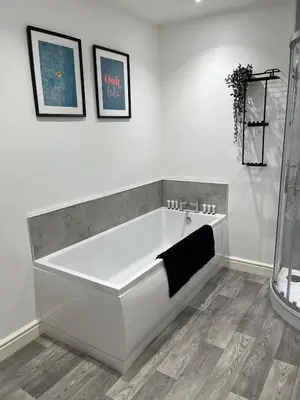 a white bath tub in a white room with two pictures at 5 Bed Home near Anglesey Abbey in Swaffham Bulbeck
